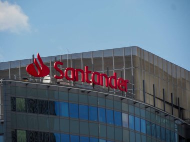 Santander Bankası 'nın canlı kırmızı logosu kentsel ufuk çizgisindeki çağdaş cam ve çelik finans merkezi üzerine aydınlatıldı