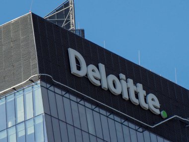 Modern ofis binasının mavi gökyüzüne karşı koyu cam cephe üzerine Deloitte profesyonel servis logosu