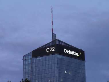 Varşova iş bölgesinde alacakaranlık mavisi gökyüzüne karşı Deloitte logosuna sahip modern cam gökdelen.