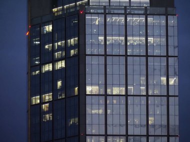 Aydınlatılmış cam ofis kulesi alacakaranlık gösteriminde şebeke desenli cephe modern şirket mimarisi
