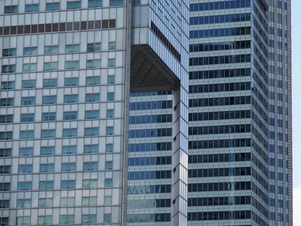 Şehir siluetine karşı geometrik pencere desenli günışığını yansıtan modern mavi cam gökdelen