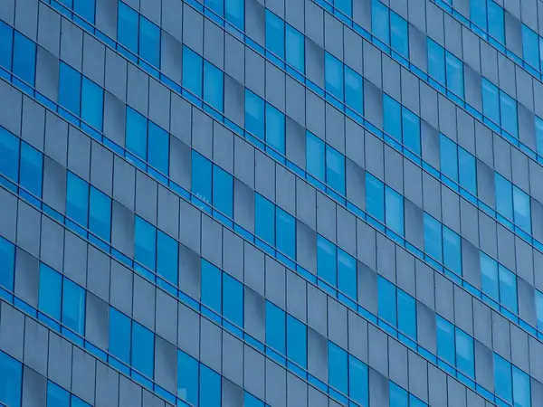 Mavi cam gökdelenin soyut deseni bulutları ve gökyüzünü yansıtıyor ve kusursuz geometrik bileşim oluşturuyor