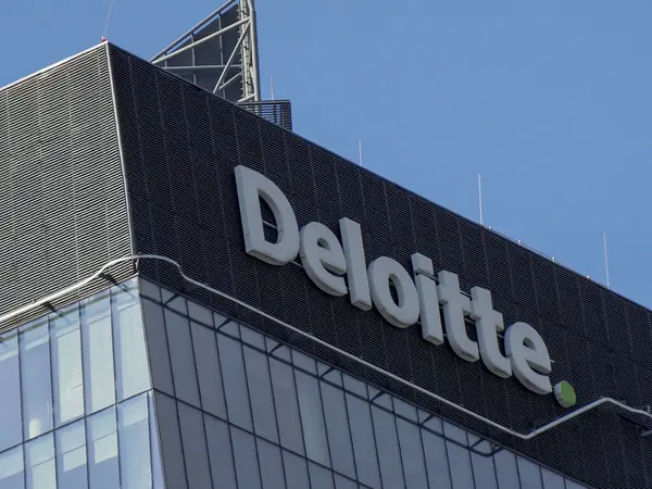 Modern ofis binasının mavi gökyüzüne karşı koyu cam cephe üzerine Deloitte profesyonel servis logosu