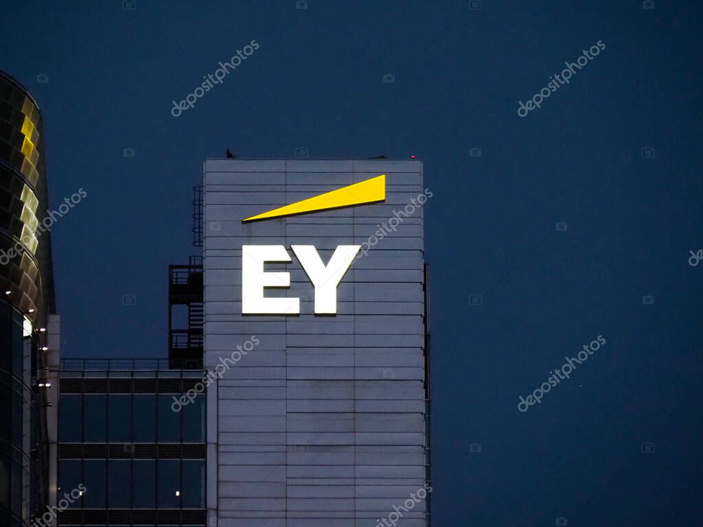 EY corporate logo illuminated on building facade against deep blue night sky in urban business district