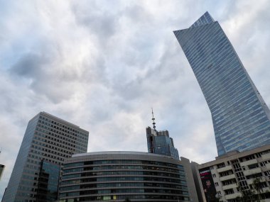 Çarpık Cam Gökdelen ve Bulutlu Gökyüzüne Karşı Ofis Binalarıyla Dramatik Kentsel Skyline