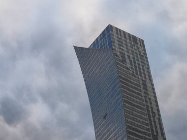 Fırtınalı gri bulutlara karşı modern gökdelenlerin dramatik açılı görüntüsü güçlü kentsel atmosfer yaratır.