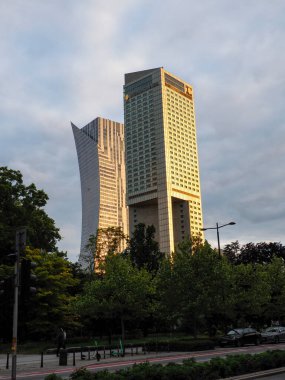 Günbatımının altın ışığı ön planda manzaralı şehir parkı olan modern gökdelenlerden yansıyor.