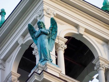 Tarihi kilise cephesinde mimari kemerlerle süslenmiş turkuaz melek heykelinin yakın çekimi.