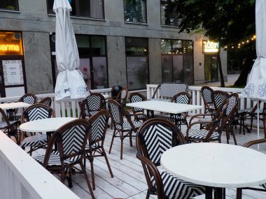 Akşam erken saatlerde zarif siyah-beyaz çizgili sandalyeleri ve yuvarlak masaları olan boş restoran terası.