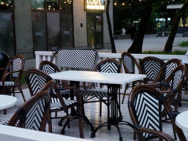 Siyah beyaz çizgili sandalyeleri ve ahşap terasta beyaz yuvarlak masaları olan şık bir açık hava kafe.