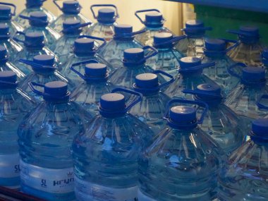 Raflarda sıralanmış mavi plastik su şişeleri perakende ortamında özdeş konteynır desenleri oluşturur