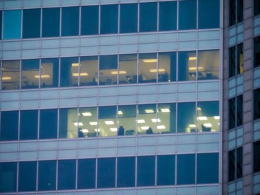 Mavi Camlı ve Aydınlatılmış Pencereli Modern Ofis Binası Gece Mesaisi Ortamı