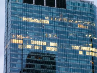 Modern ofis binasının yansıtıcı cam cephesi geometrik desenli akşam ışığı ve şehir yansımalarını yakalıyor.