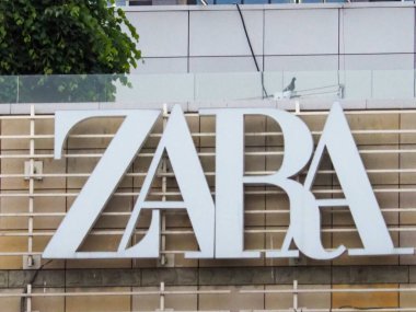 Beyaz ZARA levhası tuğla duvar cephesine asılmış yeşil yapraklar kentsel alışveriş bölgesinde görülebiliyor.