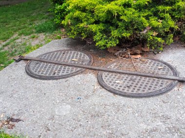 Çevresindeki yeşil bitki örtüsüyle beton kaldırımda metal rögar kapakları.