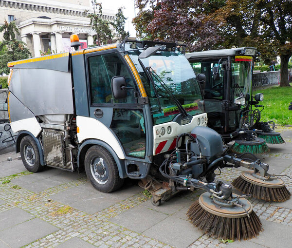 Municipal street cleaning vehicle sweeping cobblestone sidewalk in urban park area
