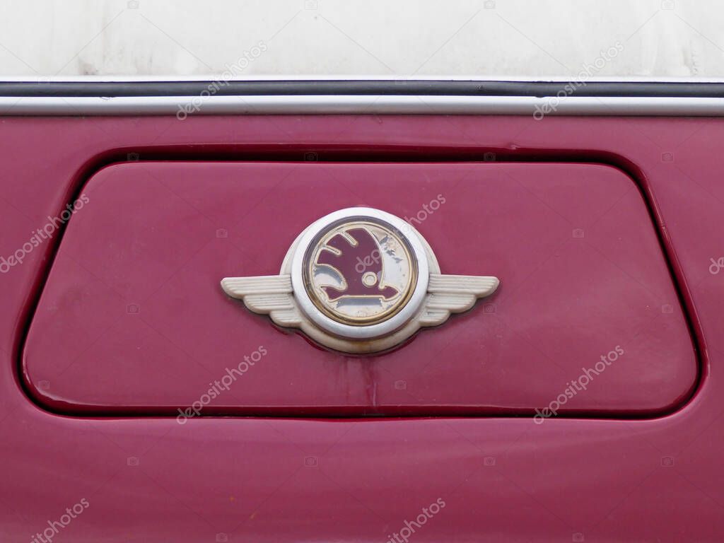 Closeup of vintage red Skoda bus emblem showing iconic winged arrow logo on crimson background