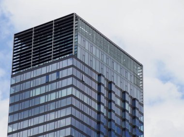 Mavi gökyüzüne ve beyaz bulutlara karşı yansıtıcı pencereli modern cam gökdelen ofis cephesi