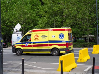 Şehir caddesinde park edilmiş sarı acil ambulans aracı tıbbi haç sembolleri ve teçhizatı görünür durumda.