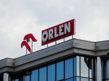 Kentsel mimaride açık mavi gökyüzüne karşı kırmızı Orlen logosu olan modern ticari bina cephesi