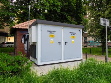 Ağaçlarla çevrili yeşil alanda güvenlik uyarıları olan modern elektrik trafo istasyonu binası.