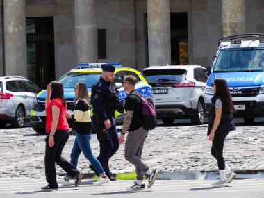 Turist grubu, polis memurları ve acil durum araçlarıyla tarihi kaldırım taşları meydanında yürüyor.