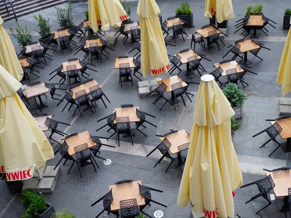 Bej şemsiyeli ve ahşap mobilyalı restoran avlusu perspektifi düzenli yemek alanları yaratıyor.