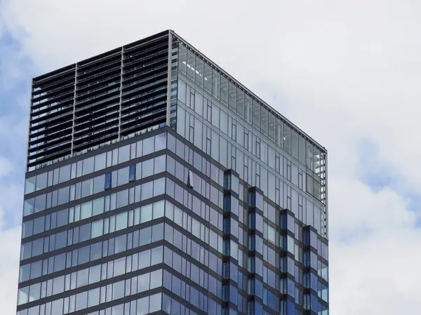 Mavi gökyüzüne ve beyaz bulutlara karşı yansıtıcı pencereli modern cam gökdelen ofis cephesi