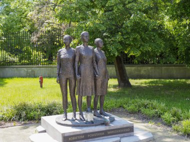 Çağdaş bronz heykel park ortamında yeşil ağaçlar ve çimlerle birlikte duran üç figürden oluşuyor.