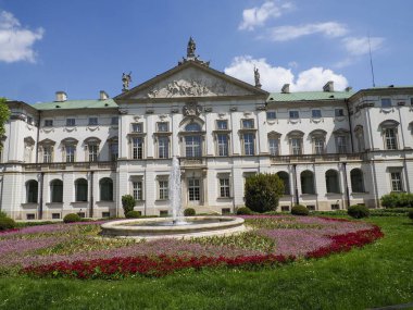 Renkli çiçek bahçeleri ve bulutlu gökyüzünün altında manikürlü çimenleri olan tarihi barok sarayı.