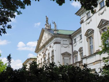 Mavi gökyüzü ve yeşil ağaçlara karşı dekoratif mimari detaylarla tarihi barok saray cephesi