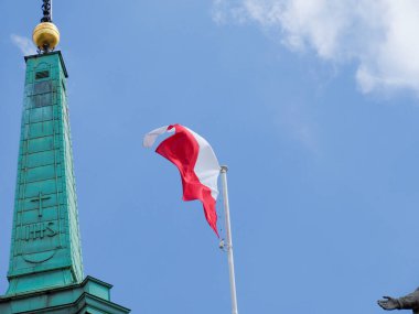Yeşil bakır kule, parlak mavi gökyüzünde dalgalanan Polonya bayrağı
