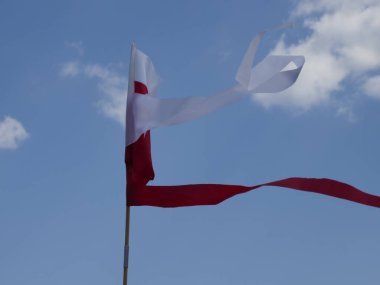 Polonya ulusal bayrağı, vatanseverlik kutlamaları sırasında beyaz bulutlu güzel mavi gökyüzüne gururla el sallıyor.