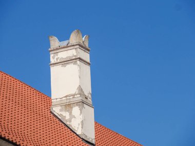 Beyaz dekoratif baca üstü parlak mavi gökyüzü ve kırmızı çatıya karşı süslü detaylar