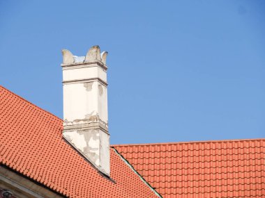 Terracotta çatı kiremitleri ve mavi gökyüzüne karşı dekoratif tacı olan geleneksel beyaz baca