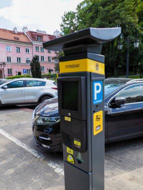 Güneşli bir günde Avrupa caddesinde park halindeki arabaların yanında duran modern sarı parkmetre.