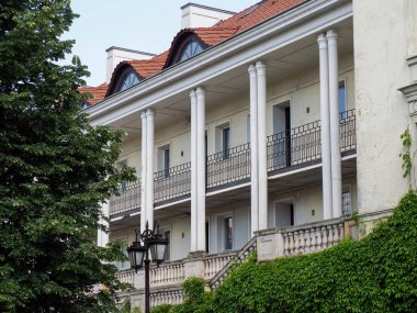 Olgun yeşil ağaçlarla çevrili sütunları ve balyaları olan klasik beyaz Avrupa konağı