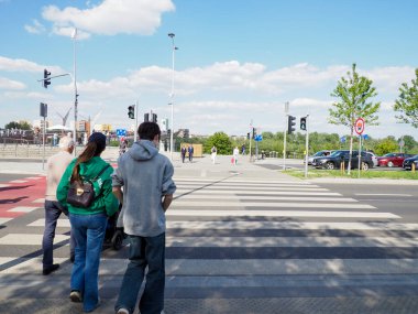 Varşova şehir merkezinde güneşli bir bahar gününde yaya geçidinde yürüyen iki kişi.