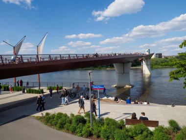 Vistula Nehri üzerindeki modern yaya köprüsünde insanlar Varşova Polonya 'da deniz kenarında gezinti yapıyorlar.