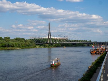 Modern Varşova köprüsünün manzarası. Geleneksel ahşap tekneler Vistula nehrinde bulutlu yaz gökyüzünün altında yüzüyor.