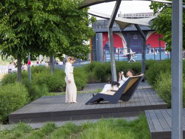 Çağdaş ahşap şezlongda oturan beyaz elbiseli modern kadın şehir parkı manzarasında