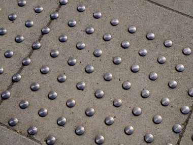 Beton kaldırım yüzeyindeki metal çivili desenler görme engelli yayalar için erişilebilirlik yolu oluşturuyor