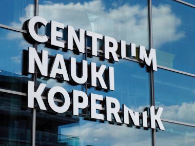 Centrum Nauki Kopernik tabelası mavi gökyüzünü ve bulutları yansıtan modern cam bina