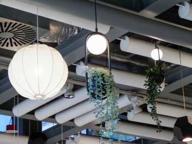 Asılı bitkileri, geometrik tavan panelleri ve modern küresel ışık kurulumlarıyla çağdaş restoran alanı