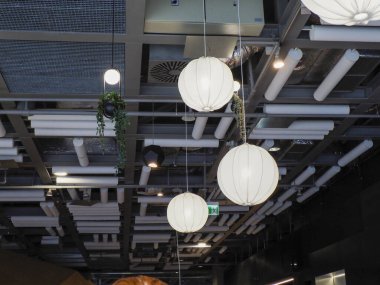 Endüstriyel modern tavan beyaz küresel aydınlatma armatürleri ve açıkta kalan havalandırma sistemi çağdaş ortam yaratıyor.