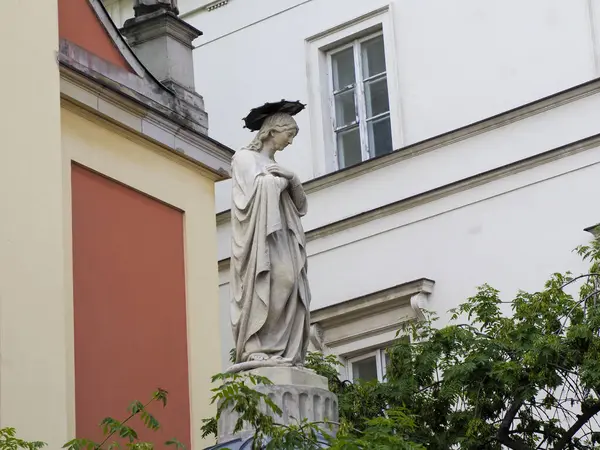 Renkli barok kilise cephesinin yanında haç yerleştirilmiş cüppeli klasik taş heykel.