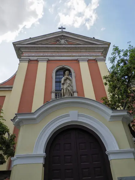 Klasik pedikürlü barok kilise girişi ve yeşil yapraklarla çerçevelenmiş kemerli kapı.