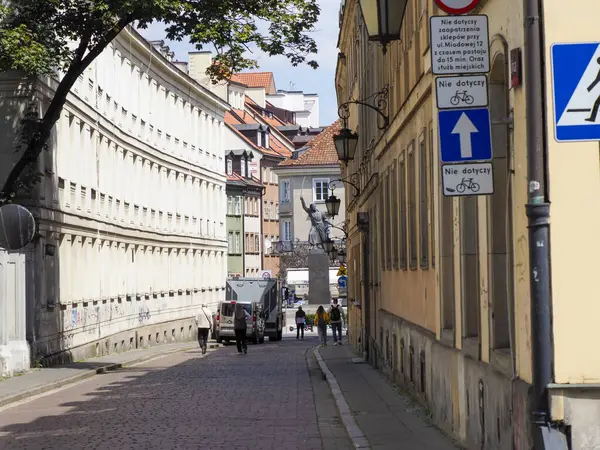 Tarihsel sarı barok sütununda güneş ışığıyla aydınlanan Avrupa avlusu mimarisinde yürüyen turistler