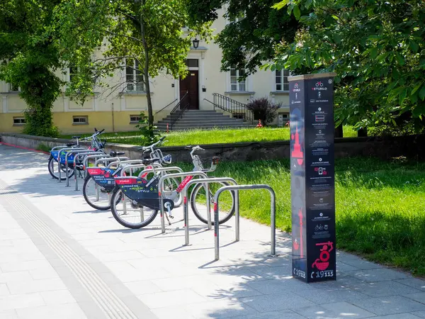 Şehir merkezinde modern binanın yanında renkli bisikletler ve yeşil peyzaj düzenlenmiş şehir bisikleti otoparkı.