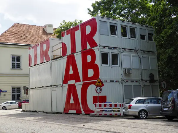 Ön planda cephe ve inşaat malzemeleri üzerine büyük kırmızı harflerle modern sanayi binası